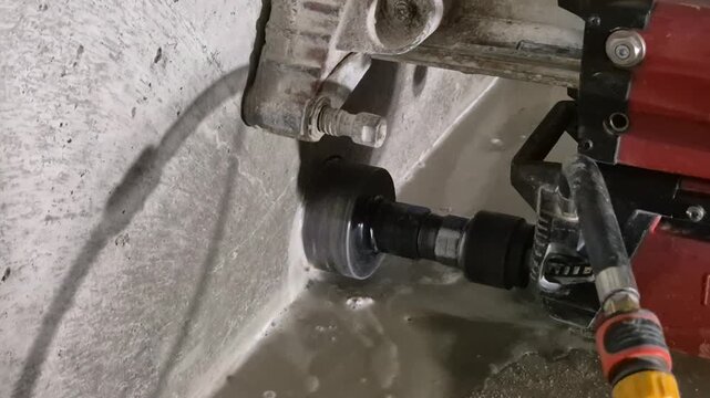 Slow motion footage of a diamond core drill machine operating in a dark basement, showing detailed concrete drilling process.