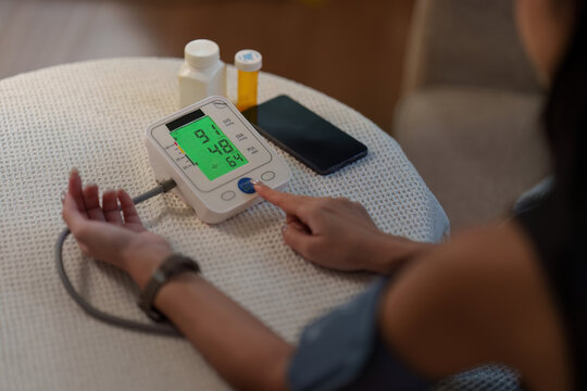 Over the shoulder view of woman checking blood pressure with digital monitor at home