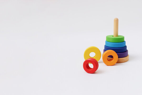 Minimalist commercial banner background with an uncompleted wooden rainbow stacking pyramid and rings on the left side, featuring large horizontal copy space on a white surface.