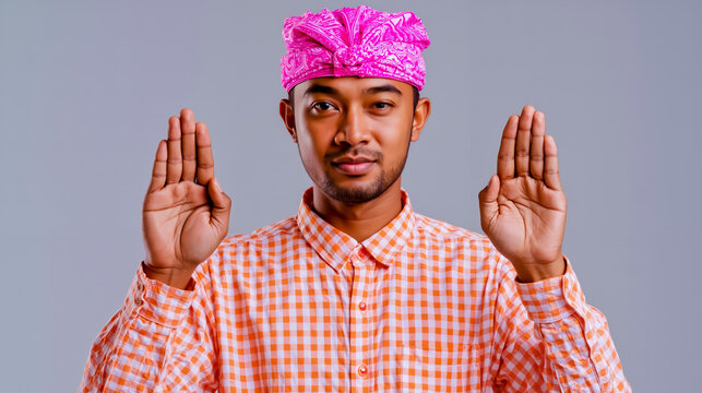 A man wearing a pink turban and an orange checkered shirt with his hands raised