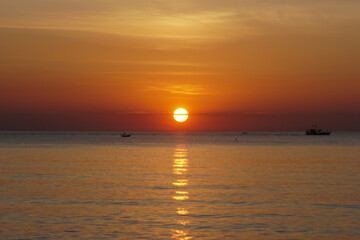 Obraz premium The red golden sun rises over the sea and fishing boats. Beautiful seascape at dawn. Bright sun rises over the horizon of the sea