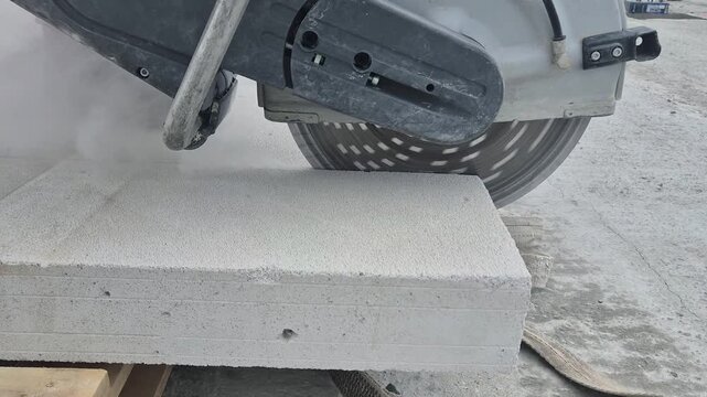 High frame rate side view of a large handheld concrete cutter circular saw cutting a non-load-bearing wall, with concrete dust dramatically flying through the air.Kateg&oacute;ri&aacute;k: Industrial / Construction