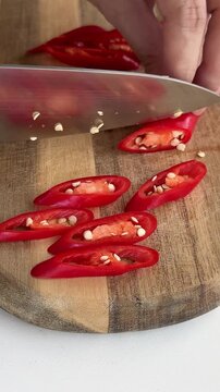 A woman is slicing red chilies on a wooden cutting board.