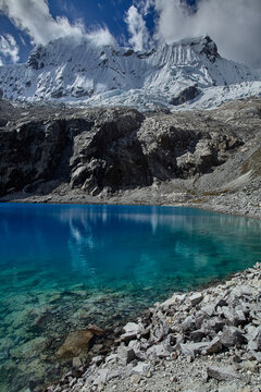 Scattered across ancient grey boulders at the shore of Laguna 69, a group of trekkers surrenders to the reward of having arrived somewhere genuinely extraordinary. Some dangle fingertips into crystall