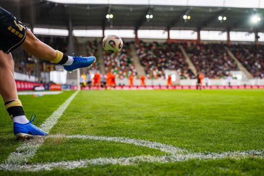 Soccer player in blue cleats taking corner kick during match, real action photo with crowd in background.