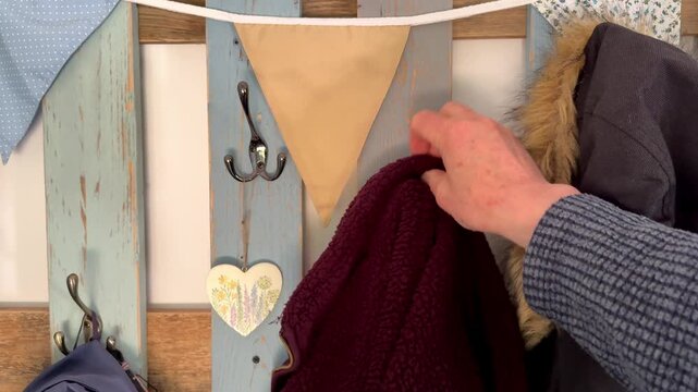 Closeup slow motion shot of a man&rsquo;s hand hanging a red fleece jacket from a hook on a basic rustic painted wooden clothes rack.