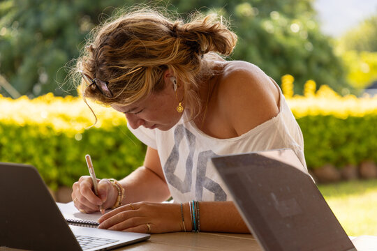young woman using laptop and writing  outdoors