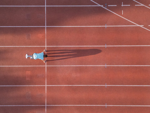 Aerial view of an athlete in starting blocks on a red running track with white lane lines and long shadows in Almere, Flevoland, Netherlands.
