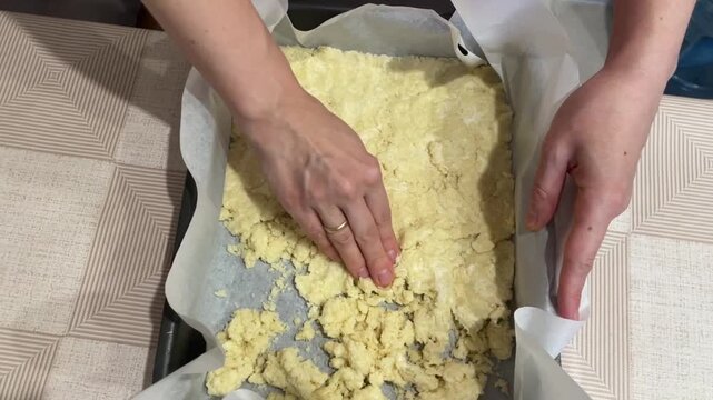 smoothing buttery crumb base into parchmentlined tray white home cook uses flat palms to level base evenly, gentle pressure forms uniform layer ready for baking, casual kitchen atmosphere