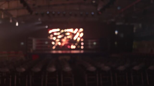Empty boxing arena with rows of folding chairs facing the ring and stage lights