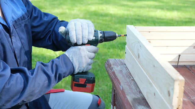 Worker man working with Screwdriver. Person using a red cordless drill with a metal spiral drill bit in a workshop, construction, diy project task. Accu battery hand drill. Screwing a screw assembling