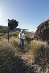 Obraz premium Woman stands on a sand dune in Gold Beach Oregon, with a strobe and softbox for a photoshoot.