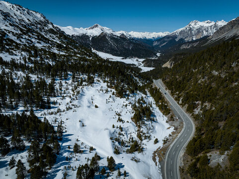 Aerial view of the winding road at Fuorn Pass surrounded by snow-covered slopes and dense pine forests in the Swiss Alps, Val Mustair, Grisons, Switzerland.