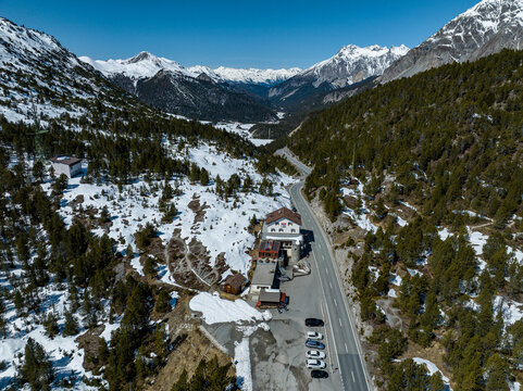 Aerial view of the Fuorn Pass mountain road and hotel building nestled among snow-dusted slopes and pine forests in the Swiss Alps Val Mustair, Grisons, Switzerland.