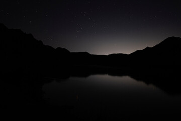 Starry night sky over a calm mountain lake and dark silhouettes of ridges. © Сергей Дудиков