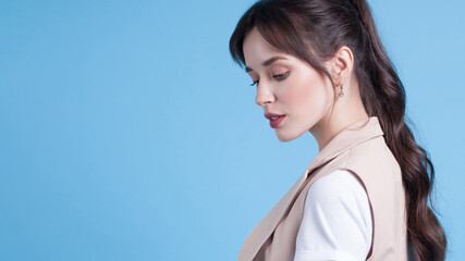 Young woman looking down posing in blue studio background © Mirrorstudio