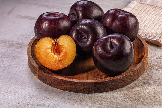 ripe dark purple plums on wooden plate with one cut open