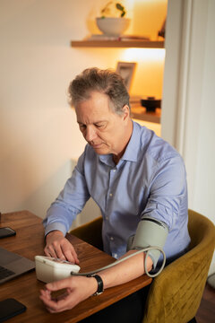 Mature man measuring blood pressure at home using digital monitor