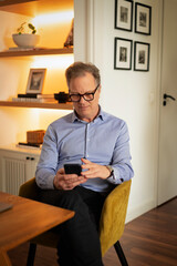 Fototapeta premium Mature man using smartphone while sitting at home
