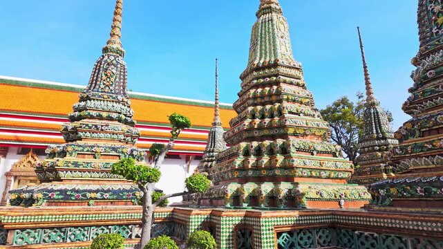 Video view of ornate stupas and Wat Pho temple in Bangkok, Thailand, highlighting richly decorated towers covered with colorful ceramic floral patterns in bright daylight.	
