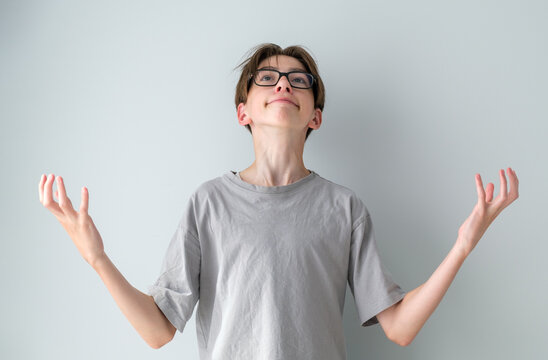 A teenager in casual clothes stands against a blue background, in an impulsive state, shouting and screaming, with his hands raised. Concept of frustration.