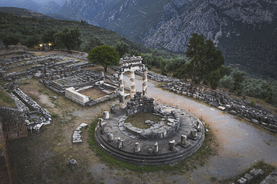 Aerial view of the ancient Tholos of Delphi at the Sanctuary of Athena Pronaia with its circular foundation and standing columns against a mountain backdrop in Delphi, Greece.