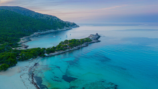 Aerial sunset view of Cala Agulla with crystal clear turquoise water and anchored sailboat, Mallorca, Spain