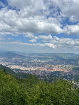 Panoramic aerial view of Sarajevo city valley surrounded by green mountains and dramatic cloudy sky from Trebevic