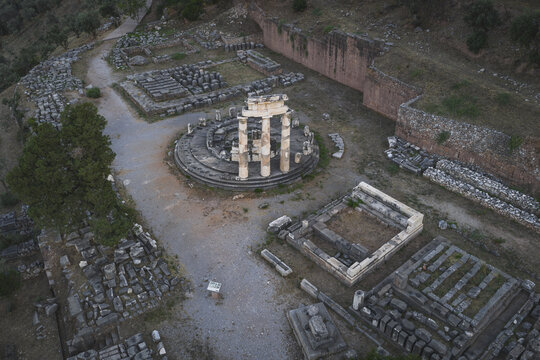 Aerial view of the ancient Tholos of Delphi featuring circular ruins and standing columns among stone foundations and lush greenery in Delphi, Greece.