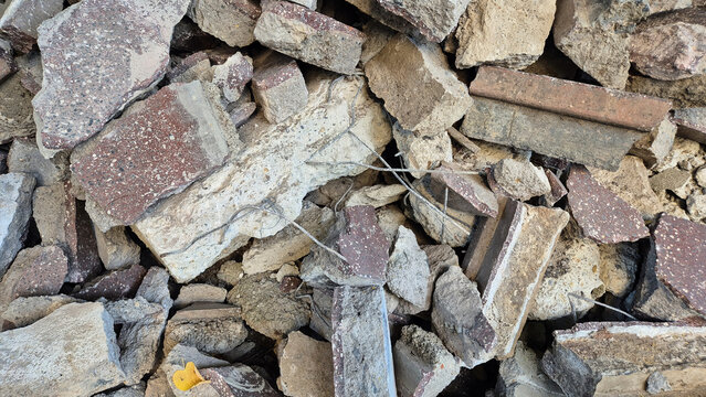 A chaotic pile of construction debris, featuring broken concrete blocks, shattered asphalt pieces, stone fragments, and exposed rebar.