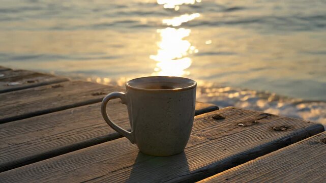 Hot Coffee Mug Steaming on a Wooden Pier by the Sea at Sunset. Seamless looping 4k video background