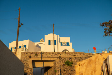 Sunlit Cycladic architecture with blue shutters above stone walls in Santorini, Greece. © Andrei Tomas