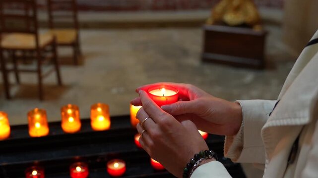 Visitor holding a glowing devotional candle among votive candles