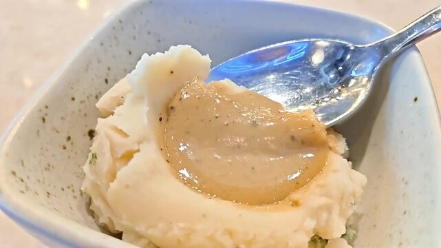 Spoon scooping up mashed potato with gravy sauce from bowl, Fluffy Side Dish, Thanksgiving Dining Serving, Creamy Rich Starch Dinner Meal, Slow Motion