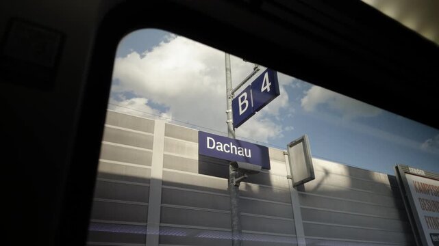 Passenger perspective view through a train window pane capturing the Dachau station sign and platform sector B4 on a sunny day in Bavaria, Germany. Perfect asset for European travel vlogs.