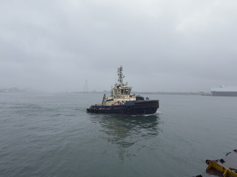 tug boat proceeding to assist the cargo ship for mooring operations during the rain weather.