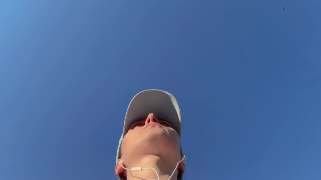 Low angle portrait of woman wearing baseball cap and headphones against clear blue sky, summer selfie outdoors