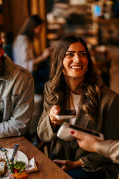 Young woman making payment with smartphone at cafe