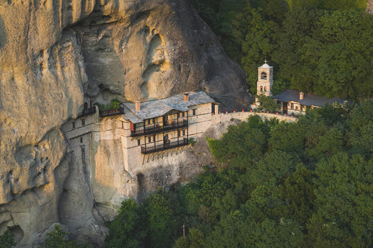 Aerial view of the Monastery of St. Nicholas Anapausas built into a steep rock cliff surrounded by dense green forest in Meteora, Trikala, Greece.