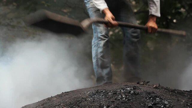 Traditional charcoal making process: A man doing hard manual labor on a burning earth kiln to produce wood coal.