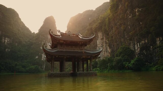 Sunset in Ninh Binh Vietnam, limestone mountains and serene waters with traditional pavilion.