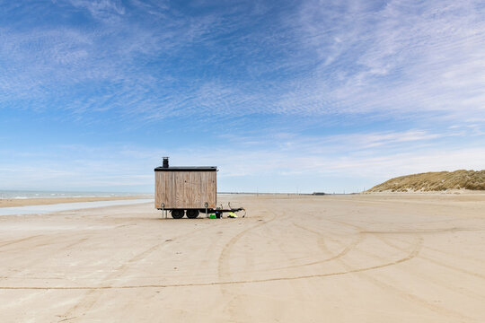 Mobile sauna on one of the beaches in Denmark lined with dunes and against a blue sky with some scattered white clouds