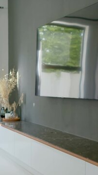 Vertical video: Panning camera revealing mirrored panel at right, exposing low cabinet and vases