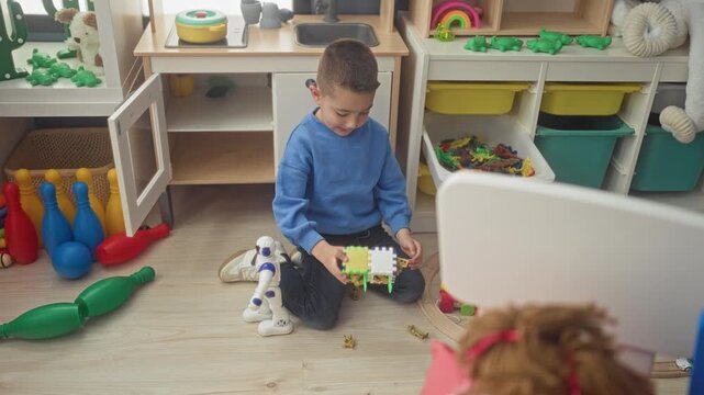 Boy holding a colorful foam puzzle cube while kneeling on a playroom floor inside a building; concentration.