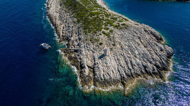 Aerial view of the rugged rocky coastline of Vis island featuring a small lighthouse and a boat anchored in the deep blue Adriatic Sea Split-Dalmatia County, Croatia.