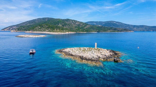 Aerial view of a small rocky islet with a stone pillar monument surrounded by turquoise Adriatic waters and a boat near the island of Vis Split-Dalmatia County, Croatia.