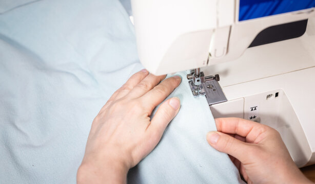 Hand guiding white fabric under sewing machine needle, sewing, crafting, needlework