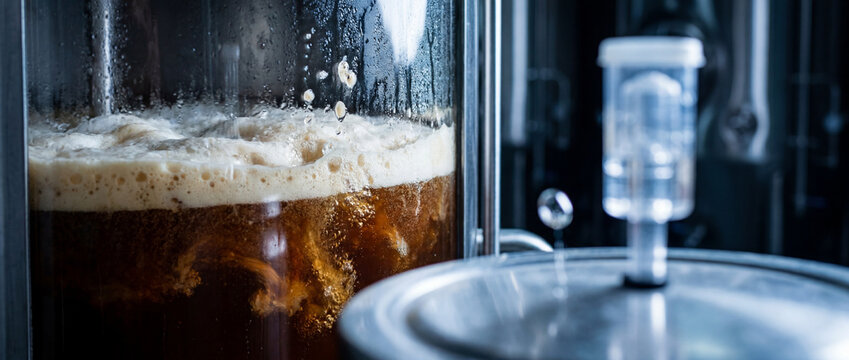 Close-up of beer fermentation in stainless steel tank with foam and brewing airlock in brewery