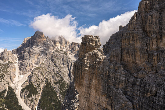 Aerial view of the Tre Cime di Lavaredo peaks with jagged rock faces and white clouds under a blue sky in Sexten, Trentino-Alto Adige, Italy.