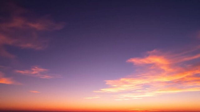 Wide angle view of a twilight sky featuring a deep purple to vibrant orange gradient with scattered wispy clouds illuminated by the setting sun at dusk or dawn horizon.